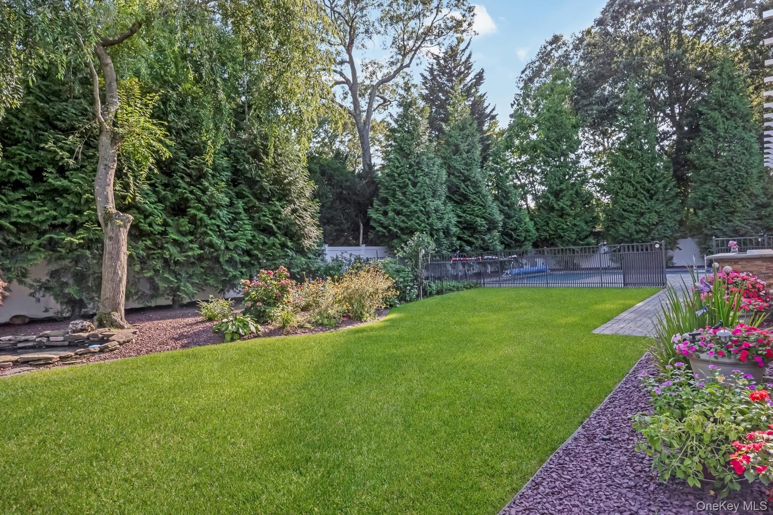 Expansive lawn area with mature perimeter trees, a paved patio, and a fenced-in pool