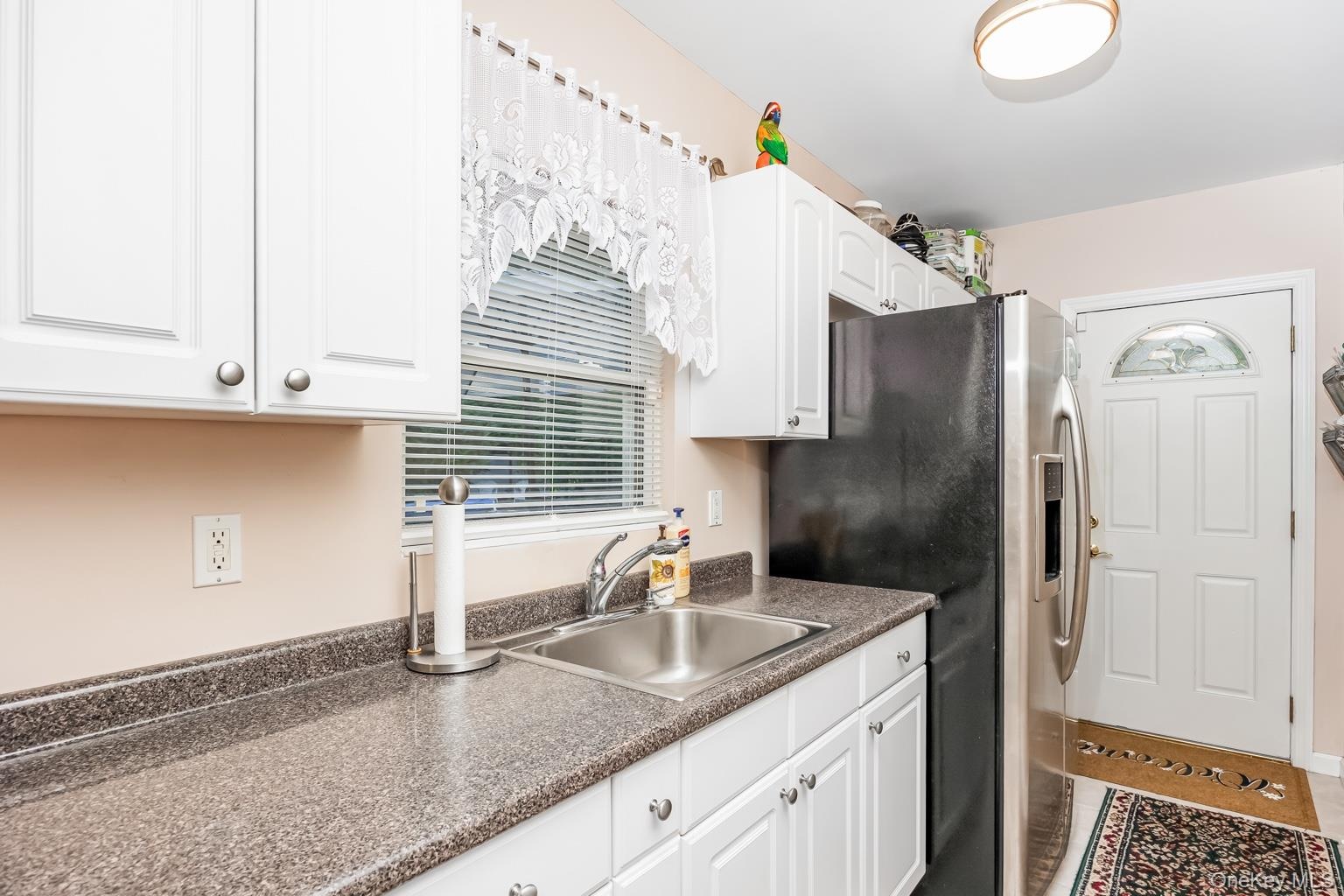 White cabinetry, a stainless steel sink, a countertop with a speckled finish, and a white paneled door with an arched glass insert