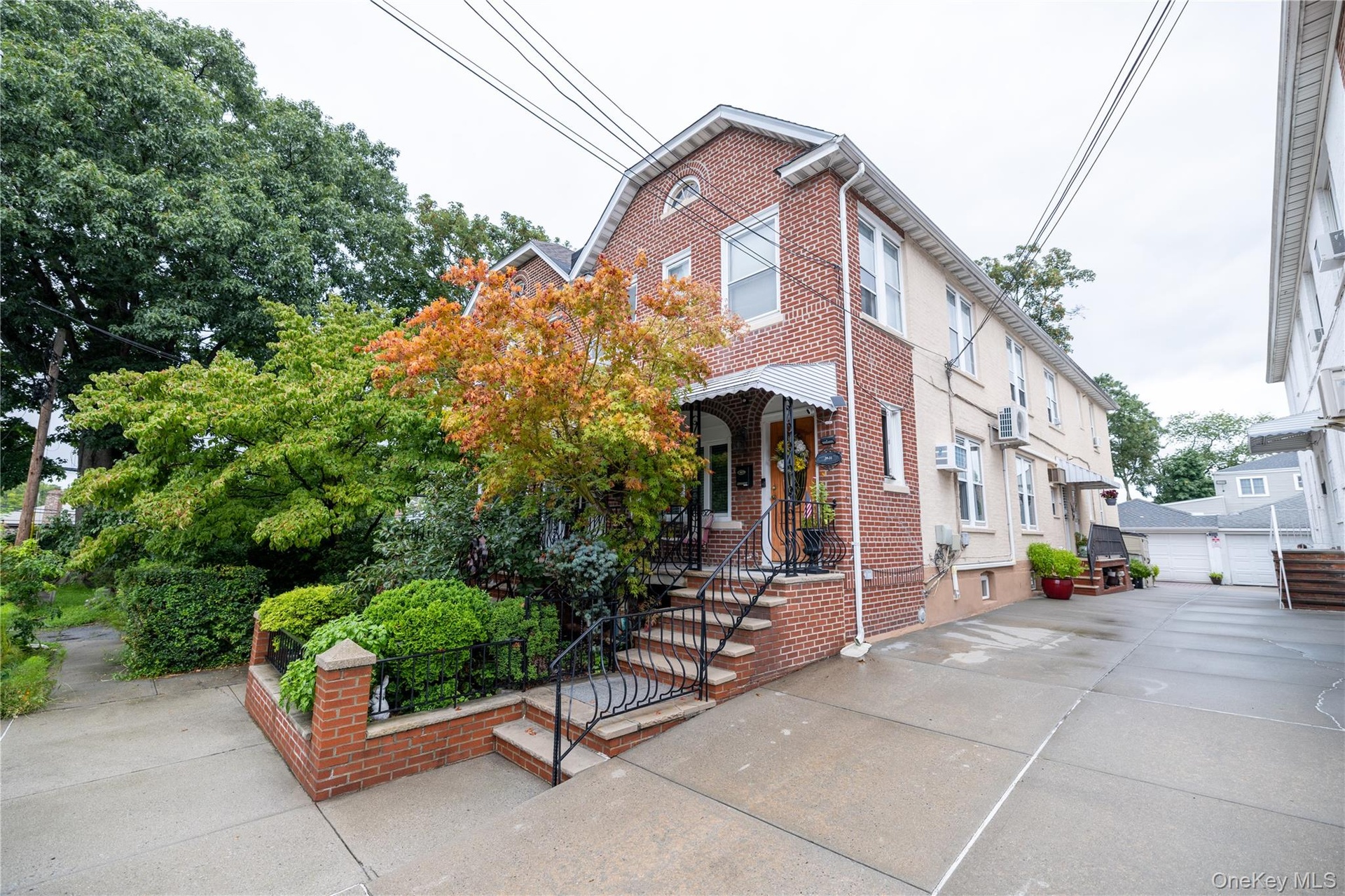 Brick and stucco exterior with multiple windows, a concrete driveway, and mature landscaping