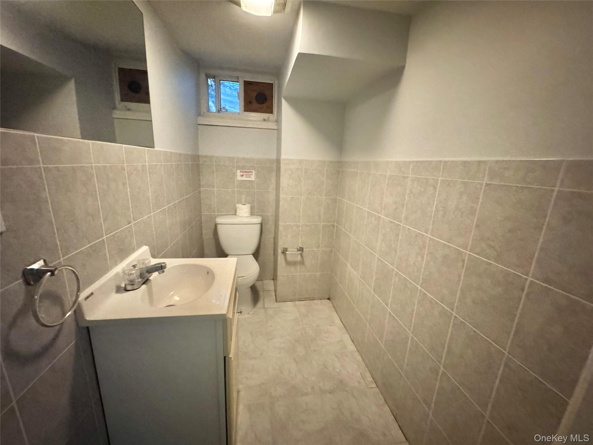 Basement Half Bathroom. Tiled walls and floor, vanity with integrated sink, and a commode