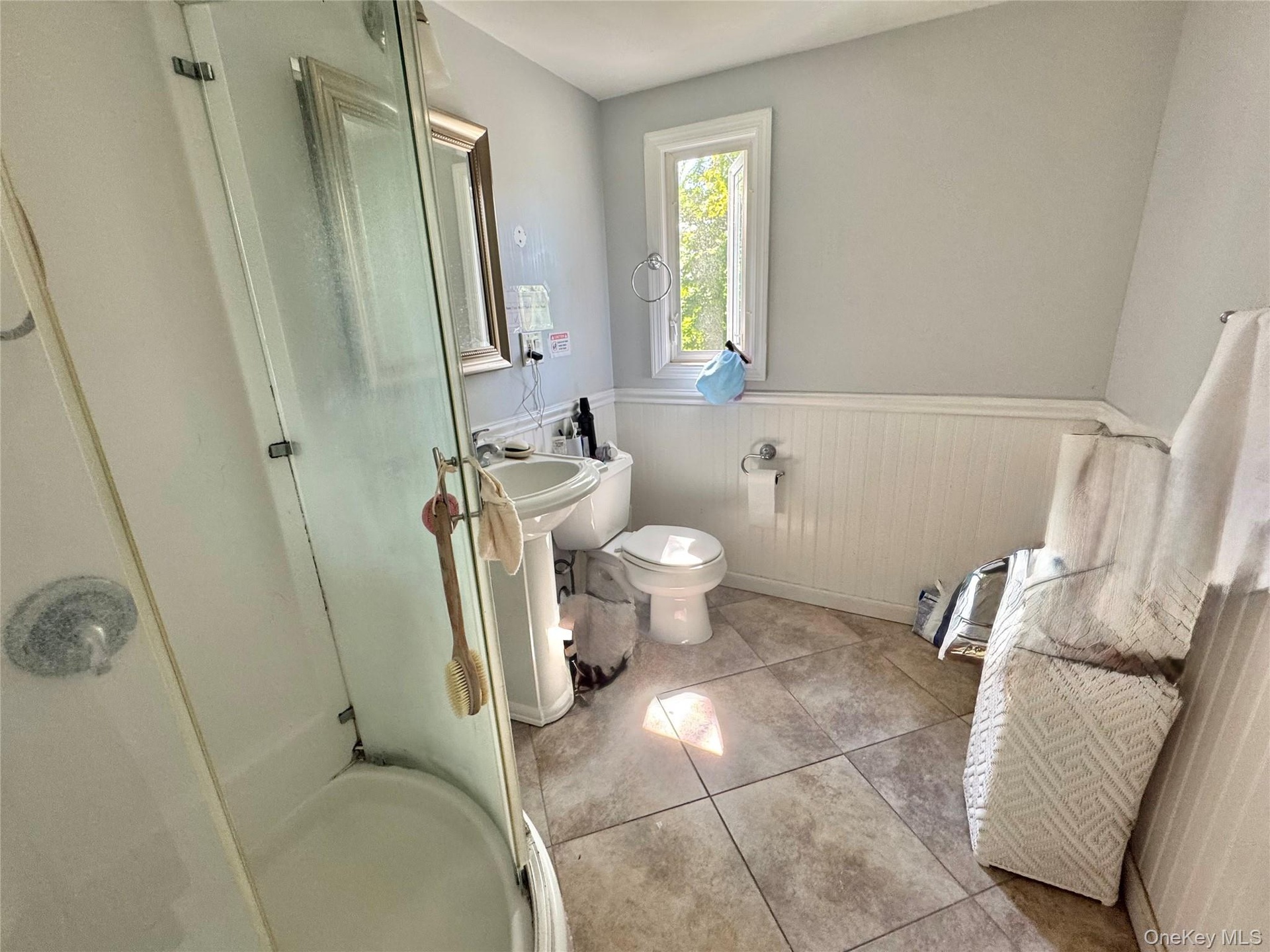 Second Floor Bathroom. Pedestal sink, tile flooring, glass-enclosed shower, white wainscoting, and a window for natural light
