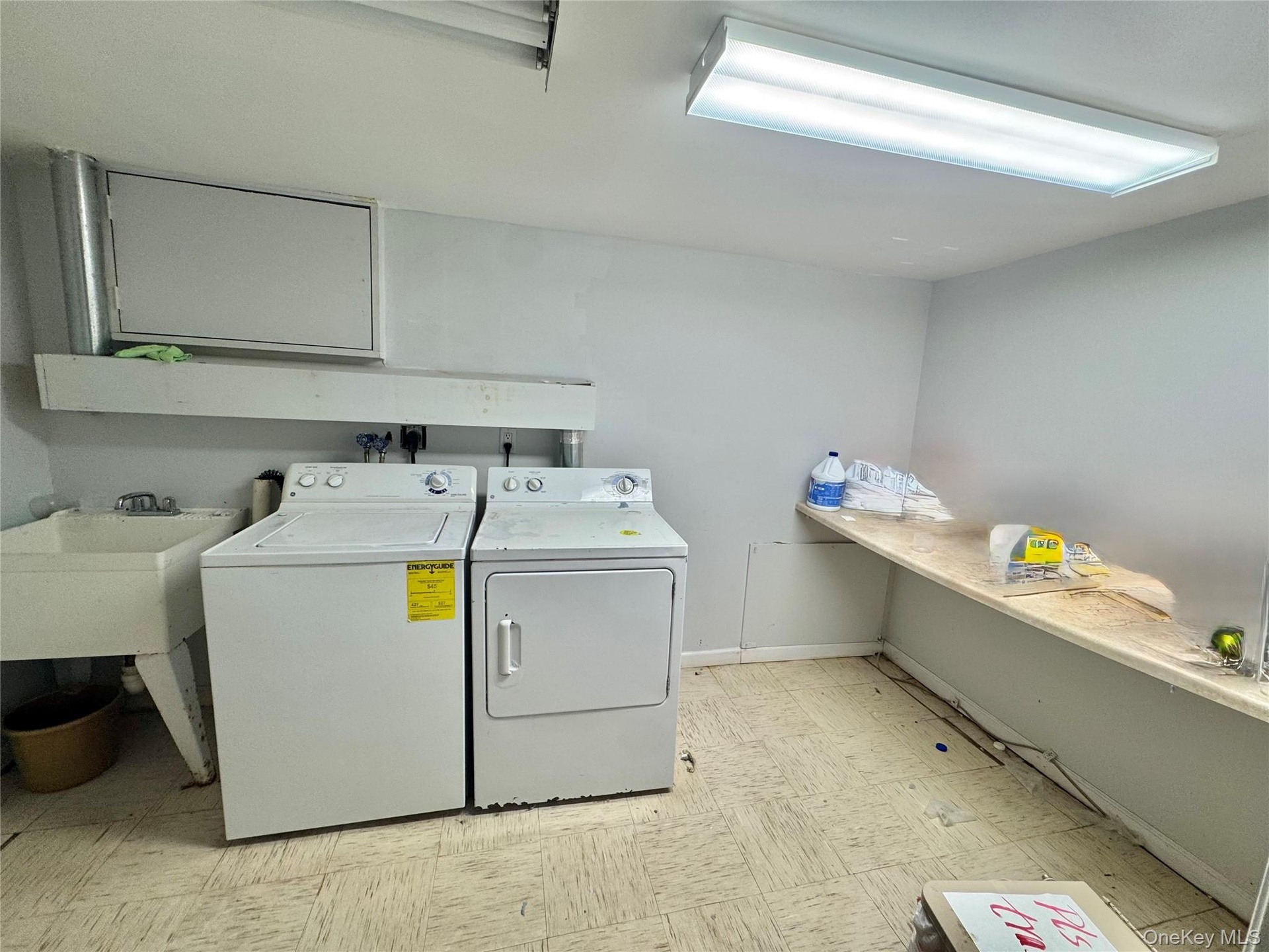 Utility room with a built-in utility sink, overhead fluorescent lighting, and a long built-in shelf