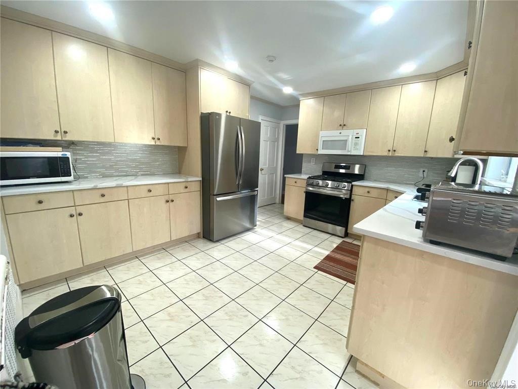 Expansive kitchen featuring light wood-finish cabinetry, stainless steel appliances, a tile backsplash, and light-colored countertops