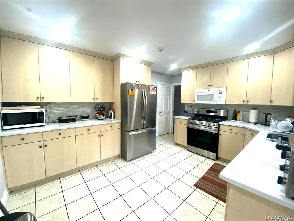Light-toned cabinetry with matching upper and lower storage, white countertops, tile flooring, and a subway tile backsplash
