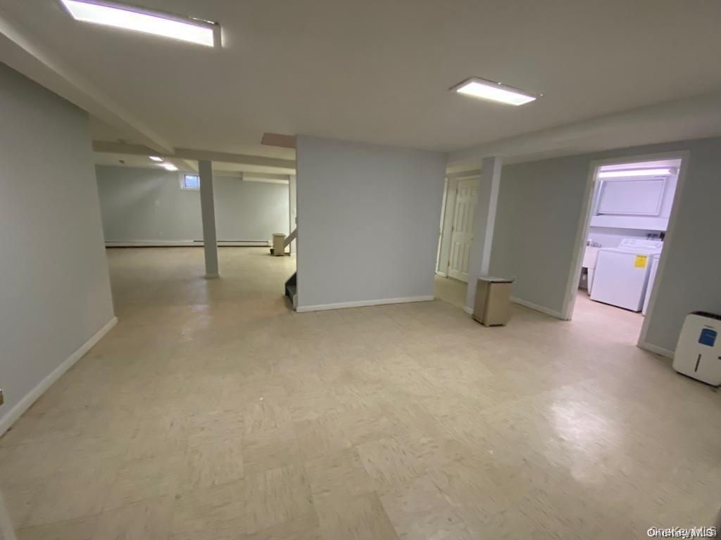 Expansive open-concept room with light-toned flooring, recessed lighting, and a dedicated laundry area featuring a stackable washer and dryer