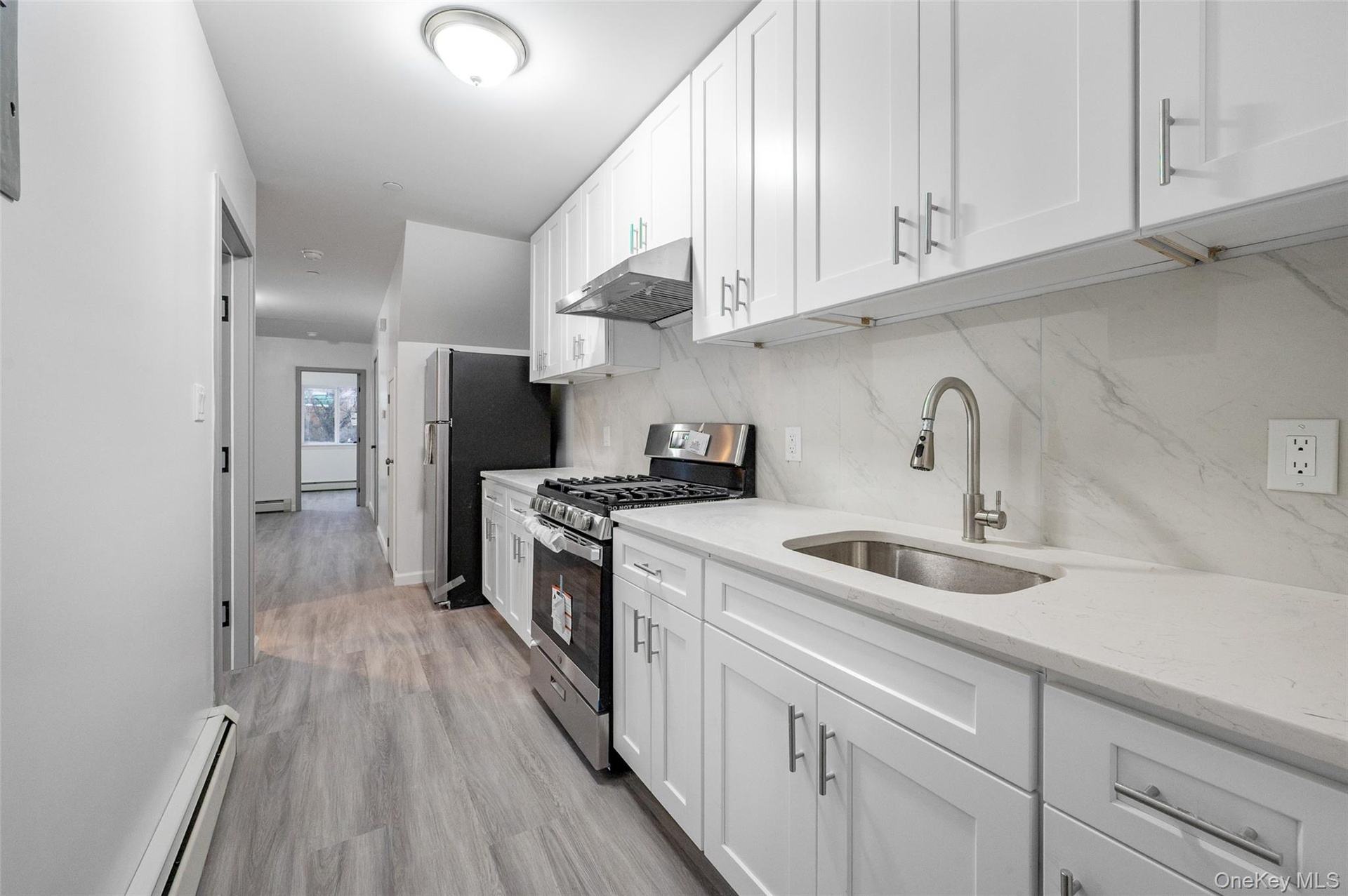 Kitchen with stainless steel appliances, a baseboard heating unit, white cabinetry, under cabinet range hood, and light stone counters