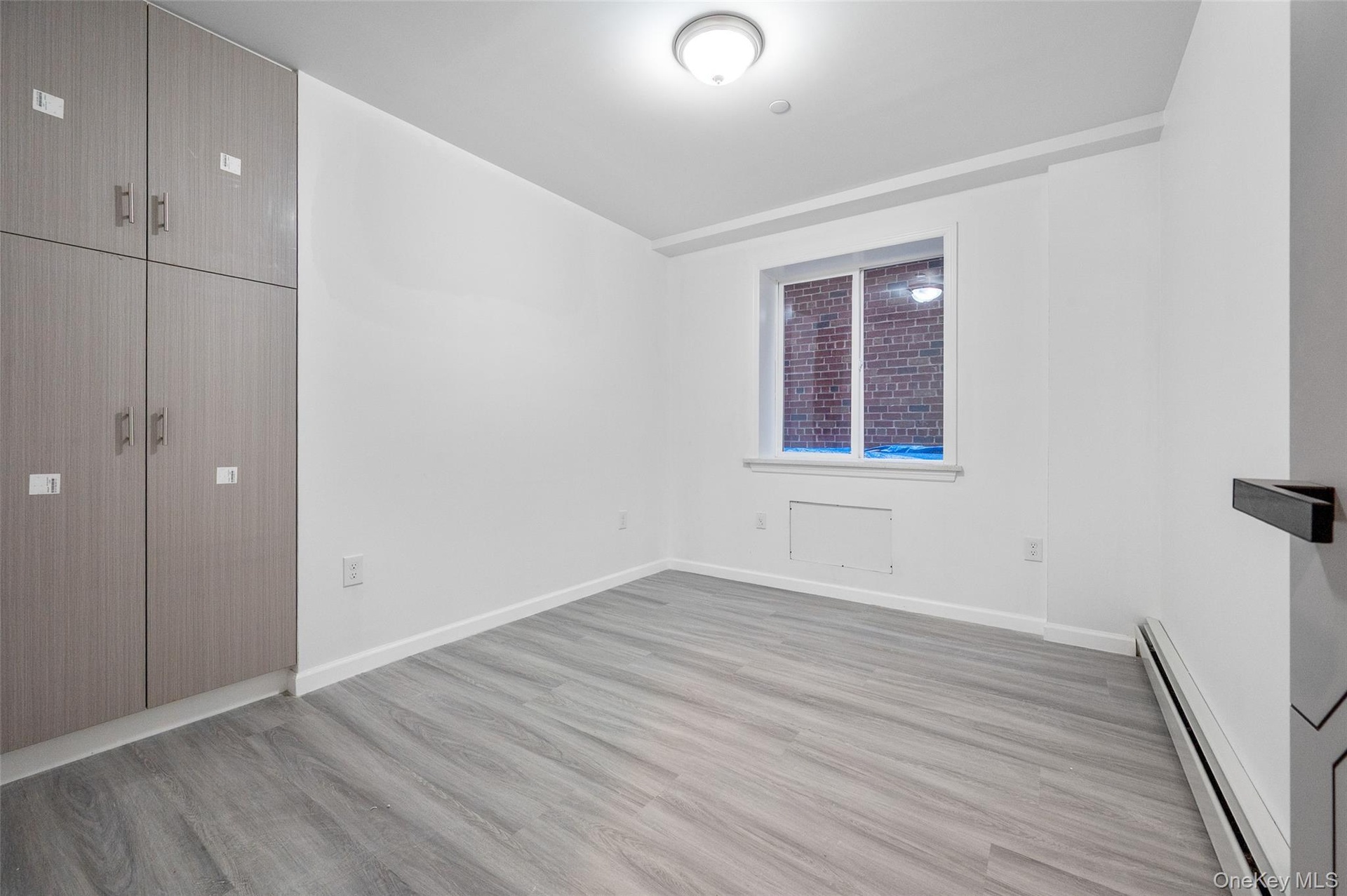 Unfurnished bedroom featuring a baseboard heating unit and light wood finished floors