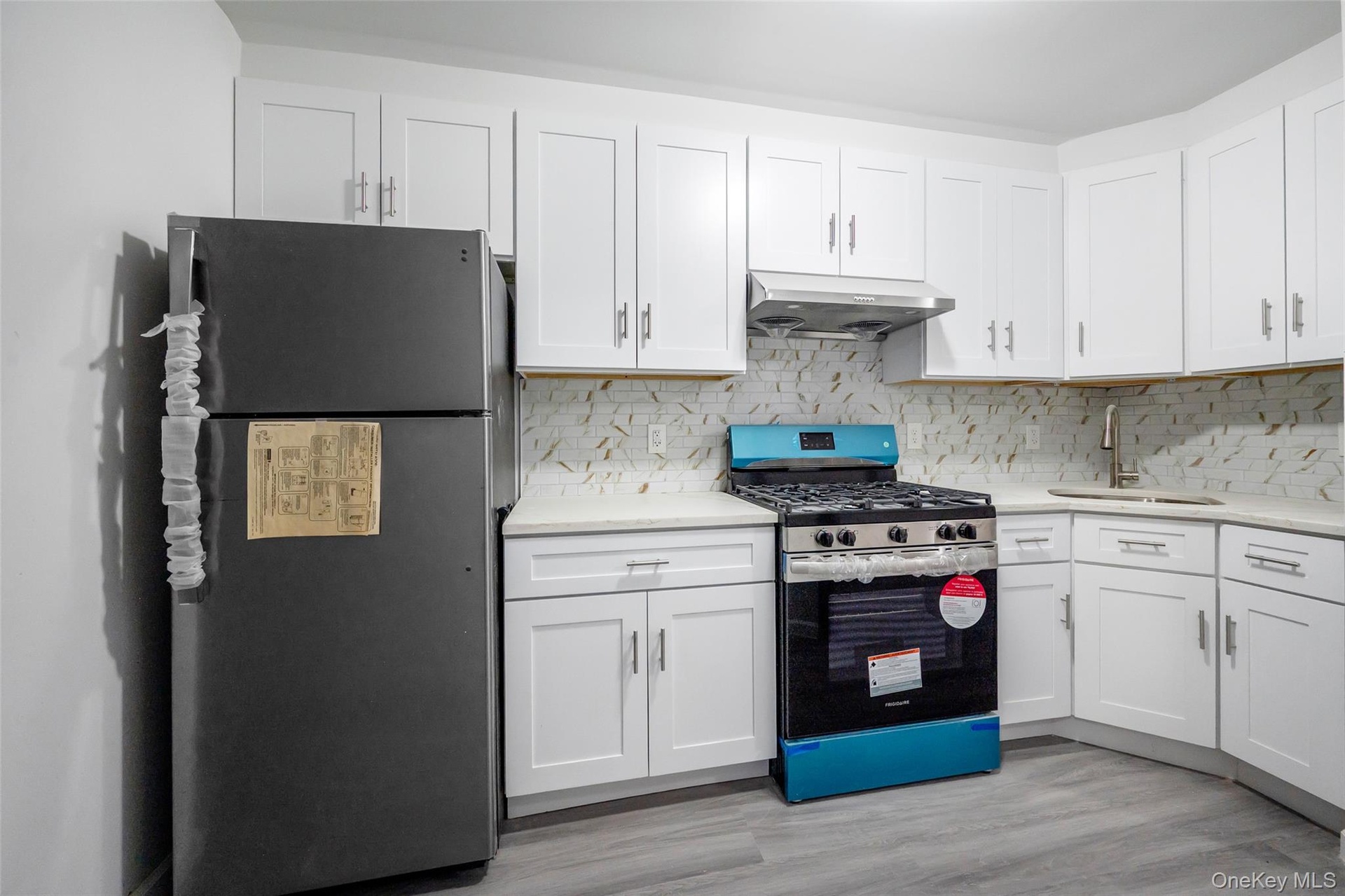 Kitchen featuring appliances with stainless steel finishes, white cabinetry, under cabinet range hood, light wood finished floors, and light stone cou