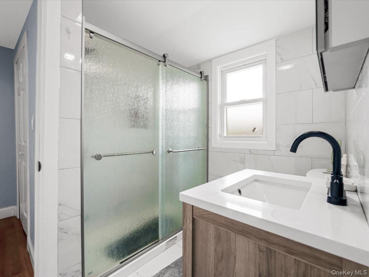 Primary Bathroom: Updated bathroom featuring a wood-finish vanity, white countertop, undermount sink, and sleek matte black faucet.