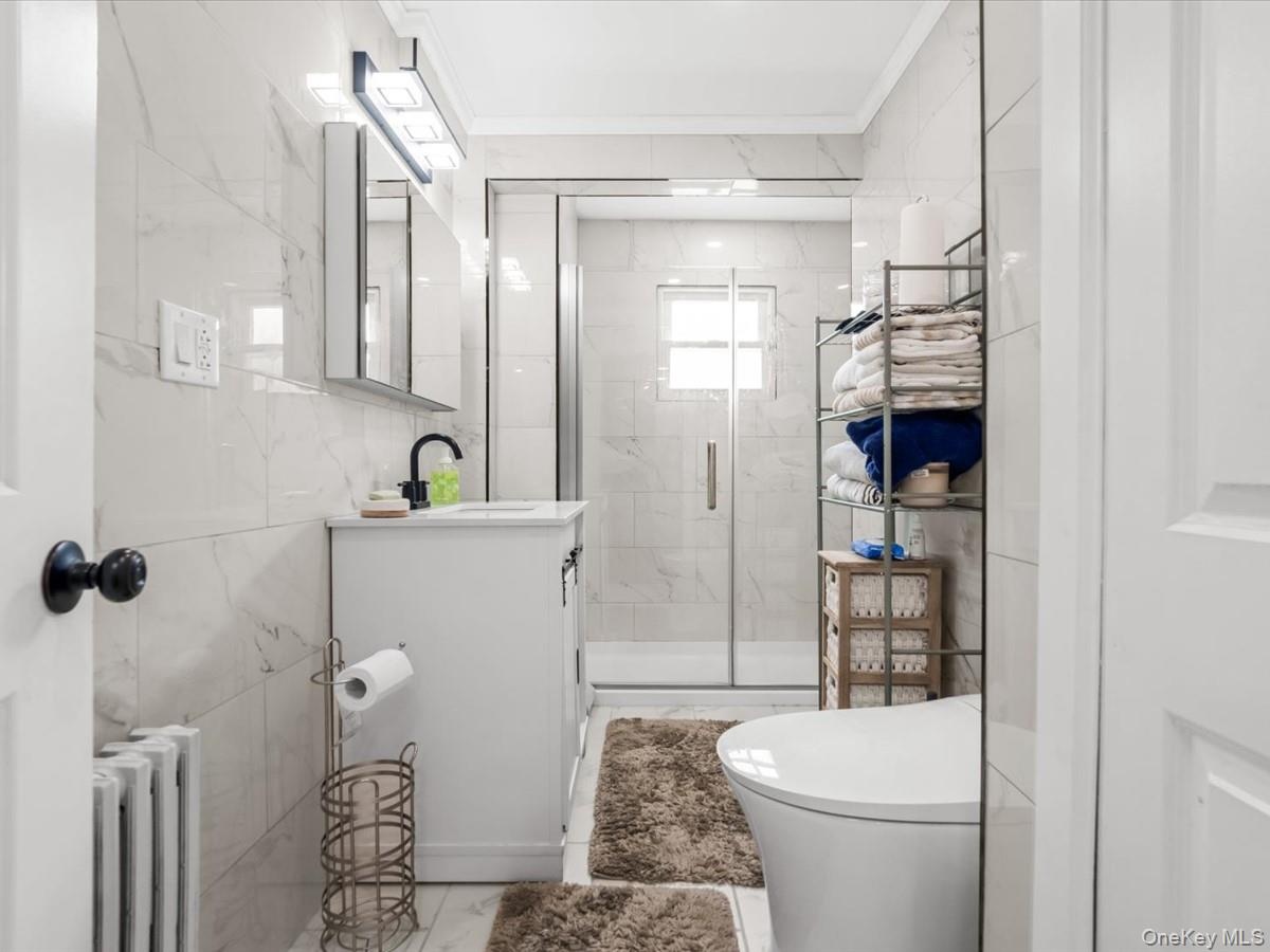 Updated full bathroom featuring a modern vanity, glass-enclosed shower, and sleek tiled finishes.