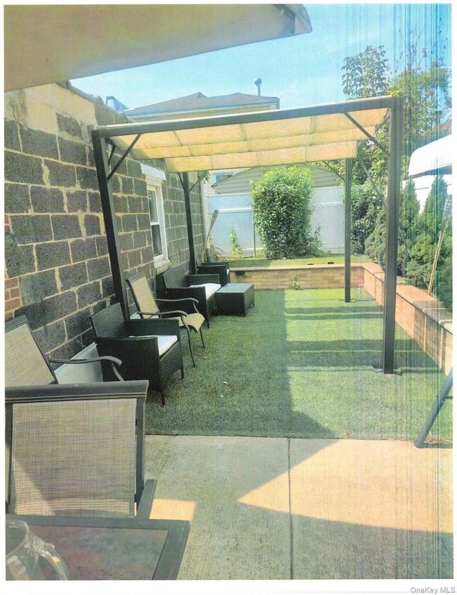 Outdoor covered patio with a retractable awning, concrete paver flooring, artificial turf, and a low brick retaining wall