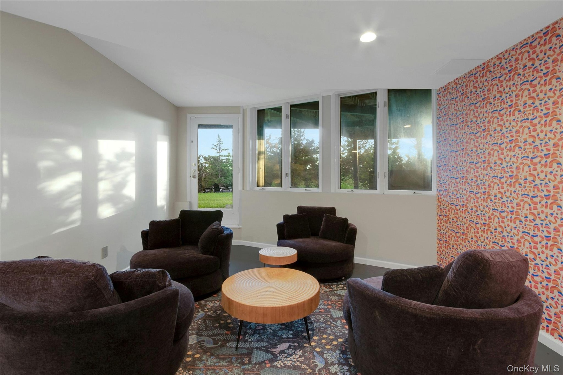 Vaulted ceiling, recessed lighting, exterior access door, a wall of multiple windows, and accent wall with patterned wall covering
