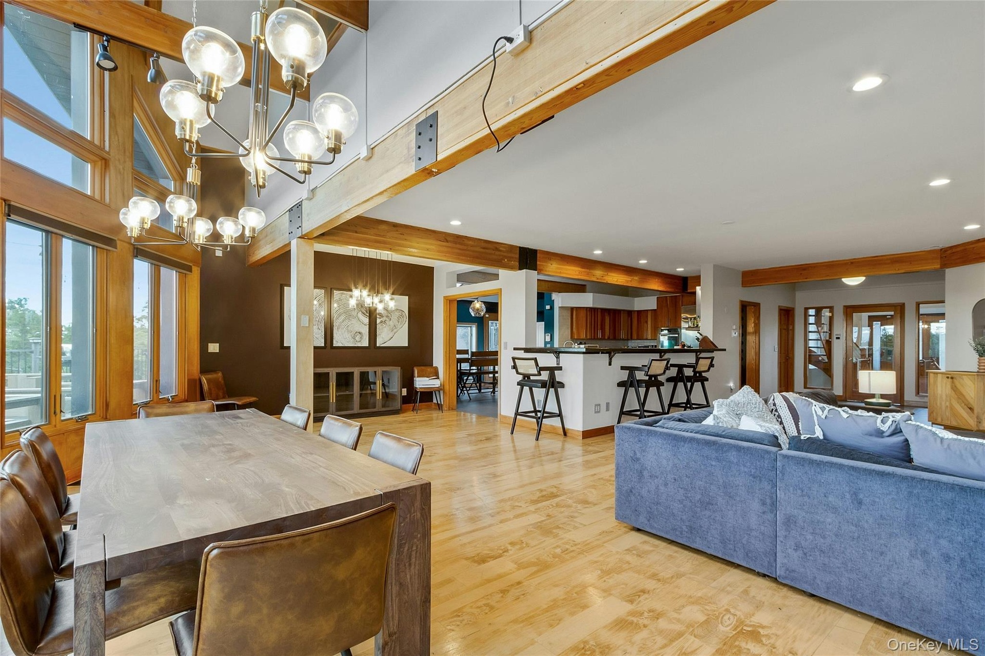 Expansive living area with wood-finish flooring, exposed wood beams, and large windows