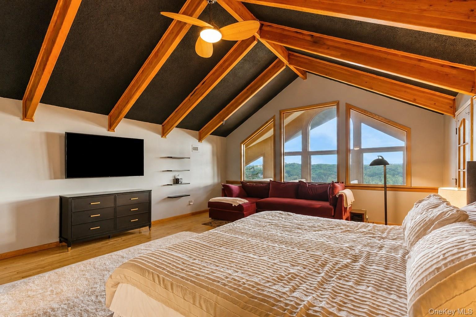 Vaulted ceiling with exposed wood beams, ceiling fan, hardwood flooring, built-in shelving, and large picture windows