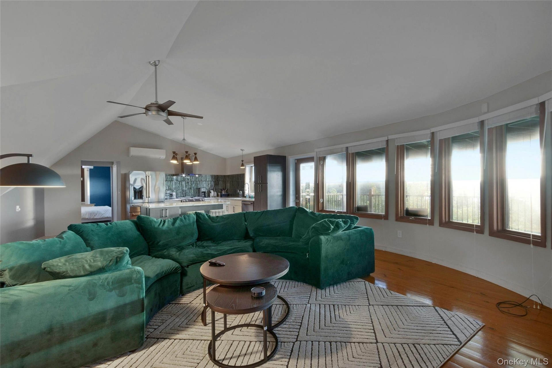 Vaulted ceiling with a ceiling fan, wood-finish flooring, and a wall of windows