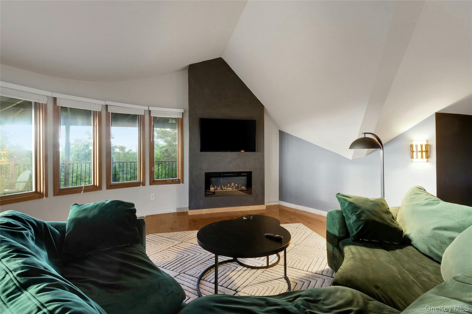 Recessed electric fireplace set in a dark-toned accent wall, light wood-finish flooring, and multiple large windows with natural wood frames