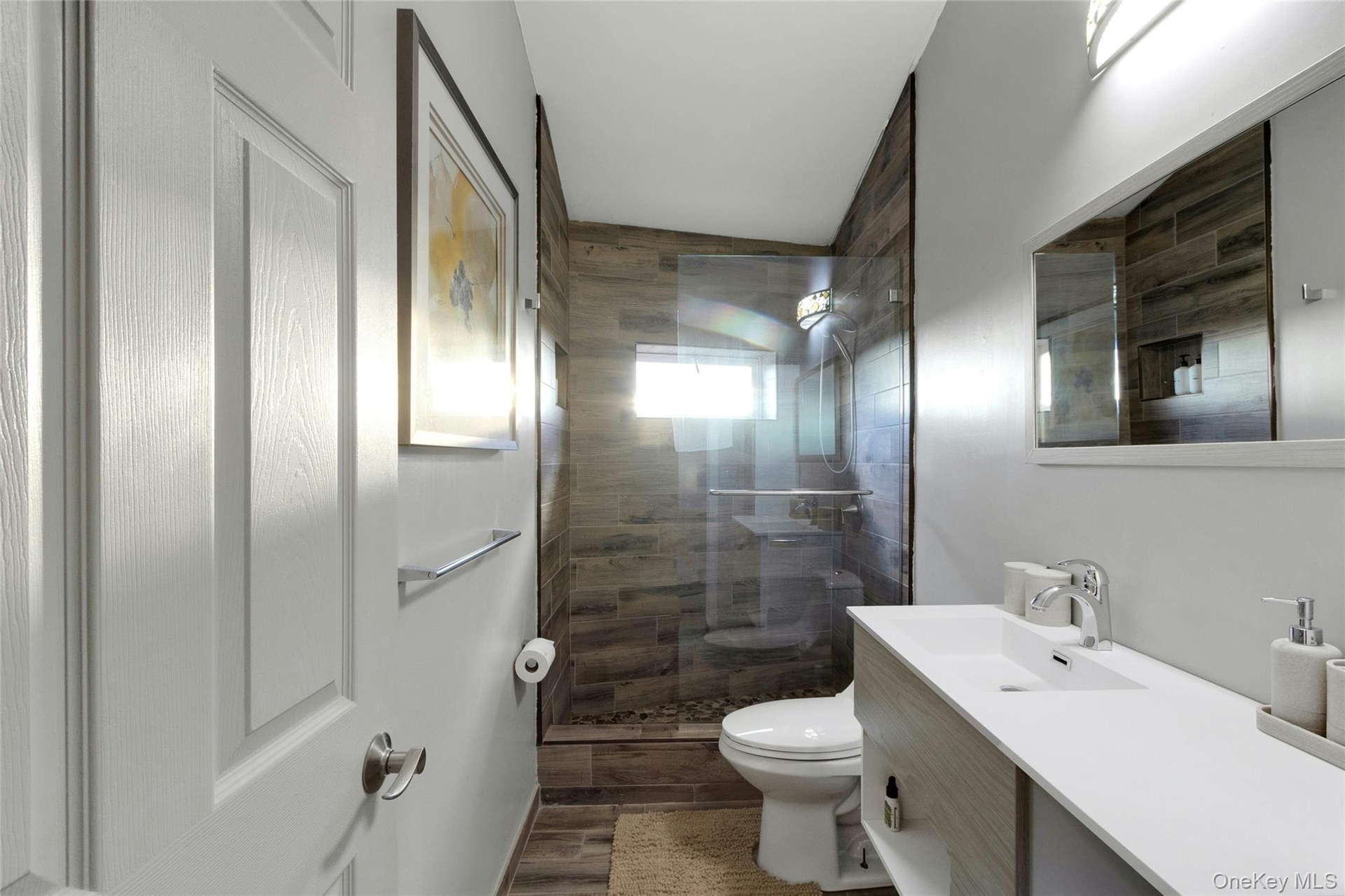 Bathroom featuring a walk-in shower with wood-finish tile surround, clear glass enclosure, and stone flooring