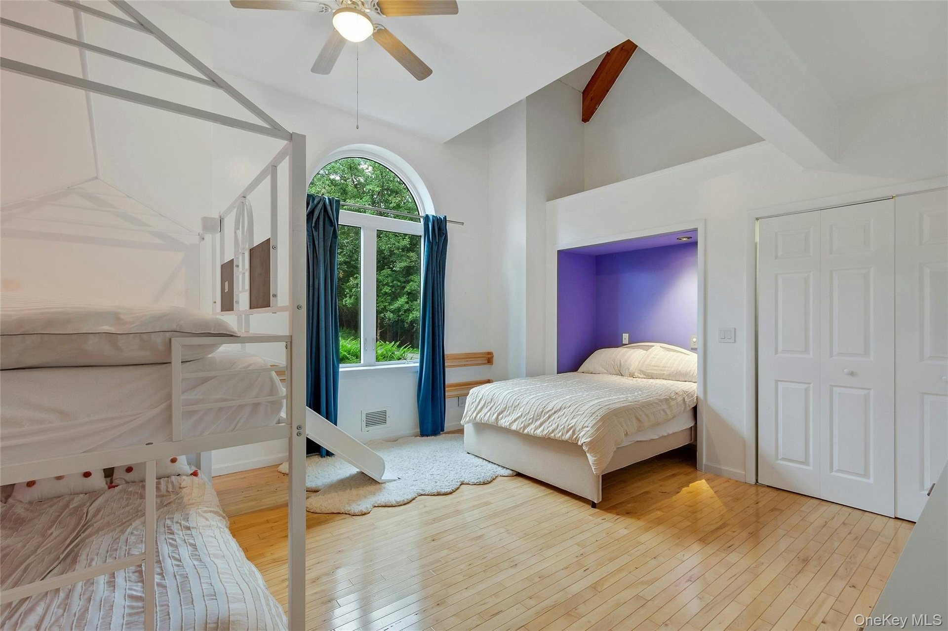 Hardwood flooring, vaulted ceilings with exposed beams, arched window, built-in bed nook, and ceiling fan