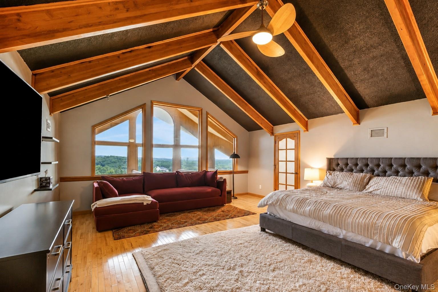 Vaulted ceiling with exposed wood beams, hardwood flooring, large transom windows, and a ceiling fan with light fixture