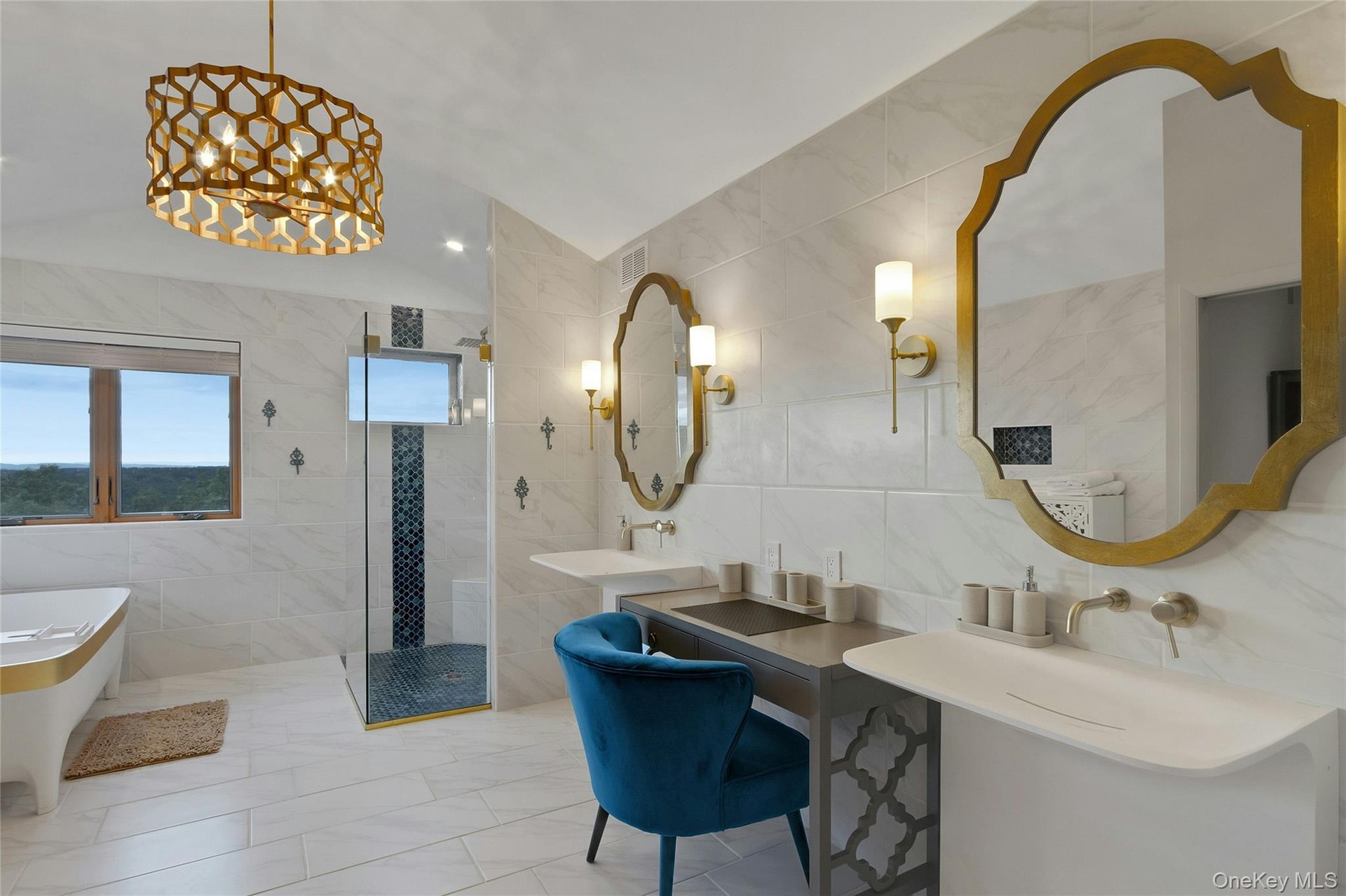 Freestanding soaking tub with gold accent, glass-enclosed shower with tiled accent wall, dual wall-mounted sinks, and ornate gold-framed mirrors