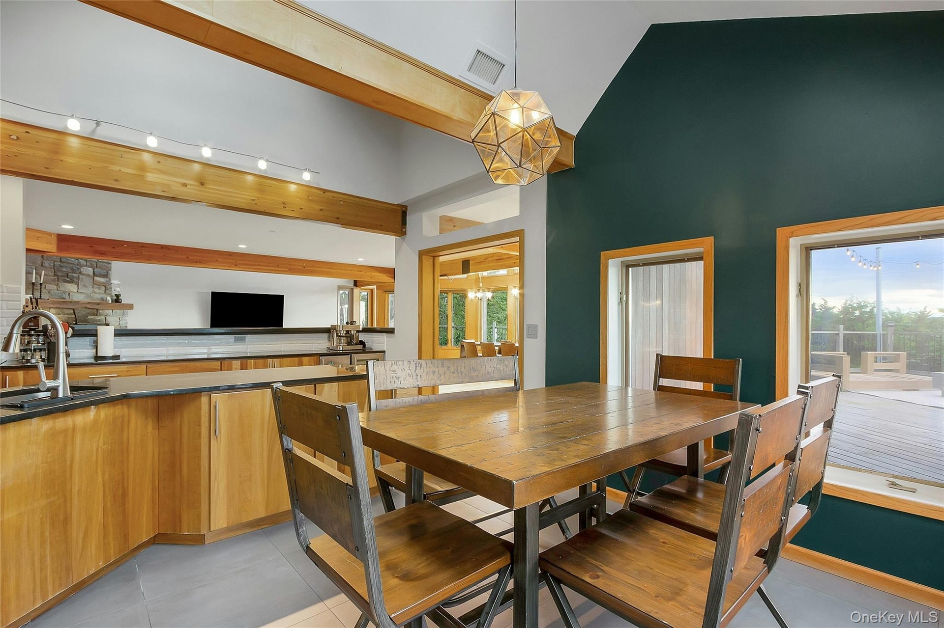 Vaulted ceiling, exposed wood beams, geometric pendant lighting, wood-finish cabinetry, and a built-in kitchen sink