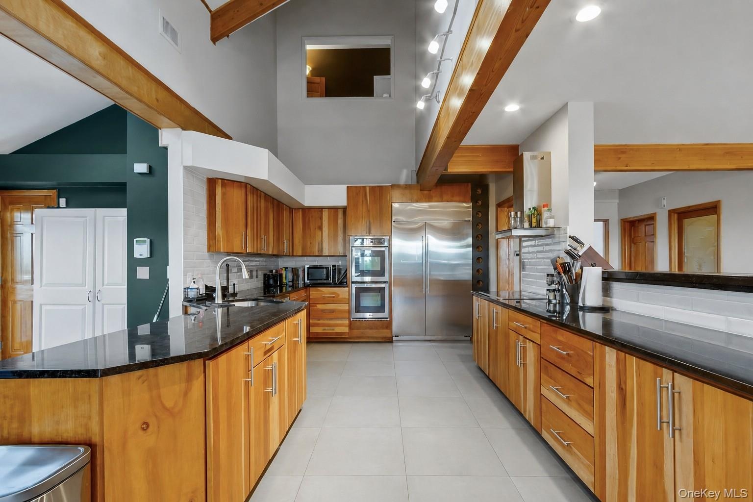 Kitchen featuring natural wood cabinetry, dark countertops, a stainless steel refrigerator, double ovens, and a tile backsplash
