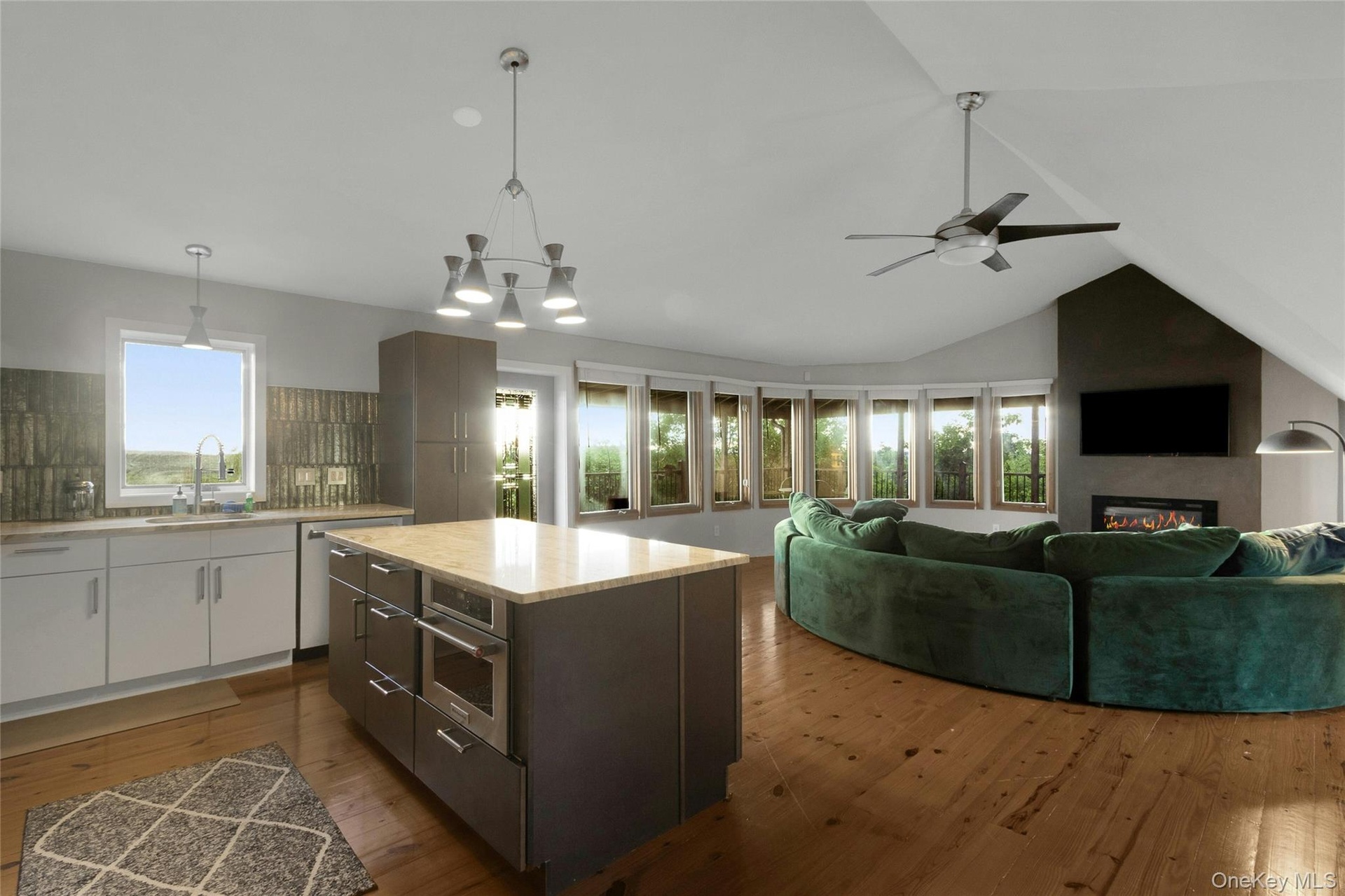 Open-concept living area featuring wood-finish flooring, a kitchen island with built-in microwave, an integrated fireplace, and a vaulted ceiling with