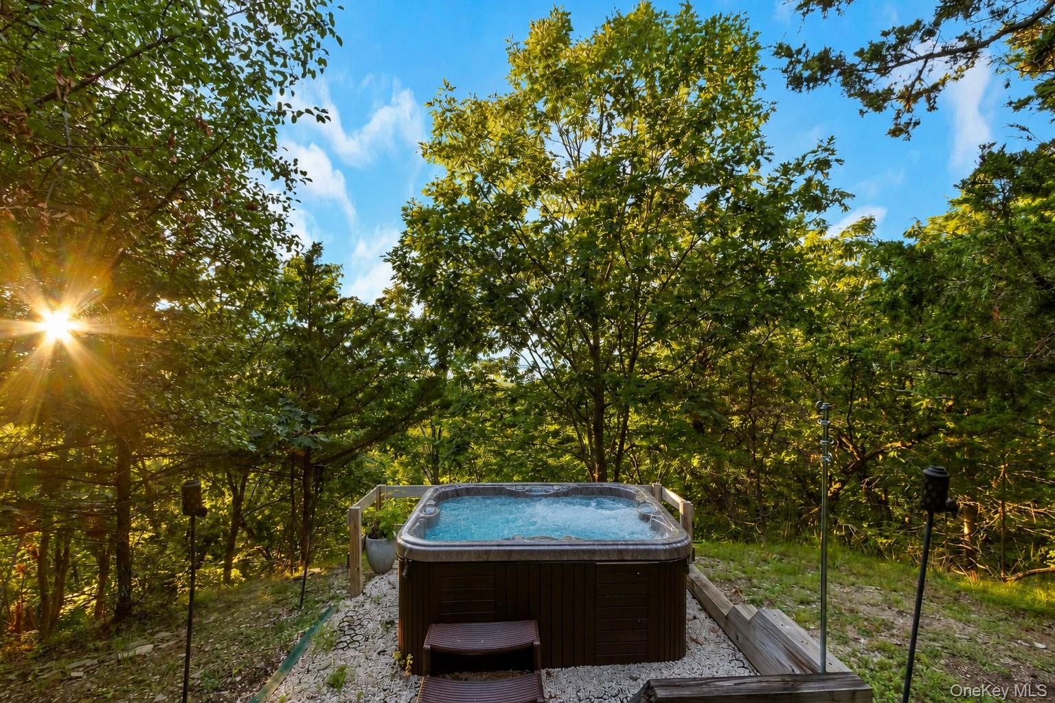 Outdoor hot tub with integrated steps, surrounded by natural landscaping and mature trees