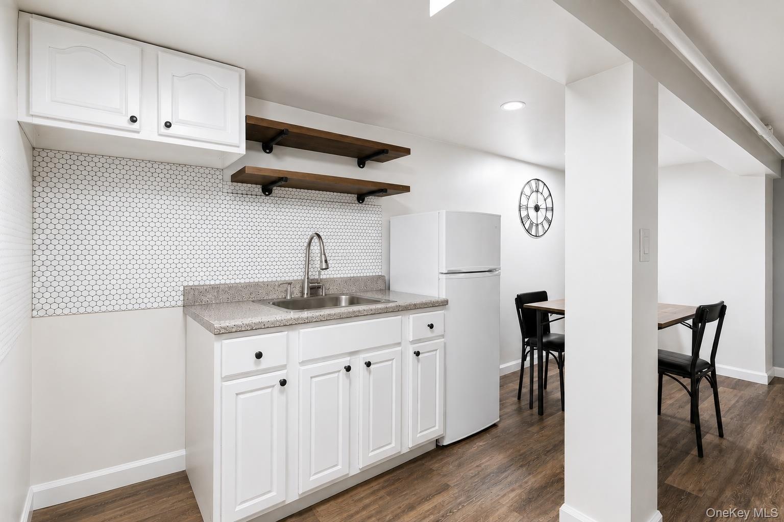 Cabinetry with black hardware, hexagon tile backsplash, wood-finish flooring.