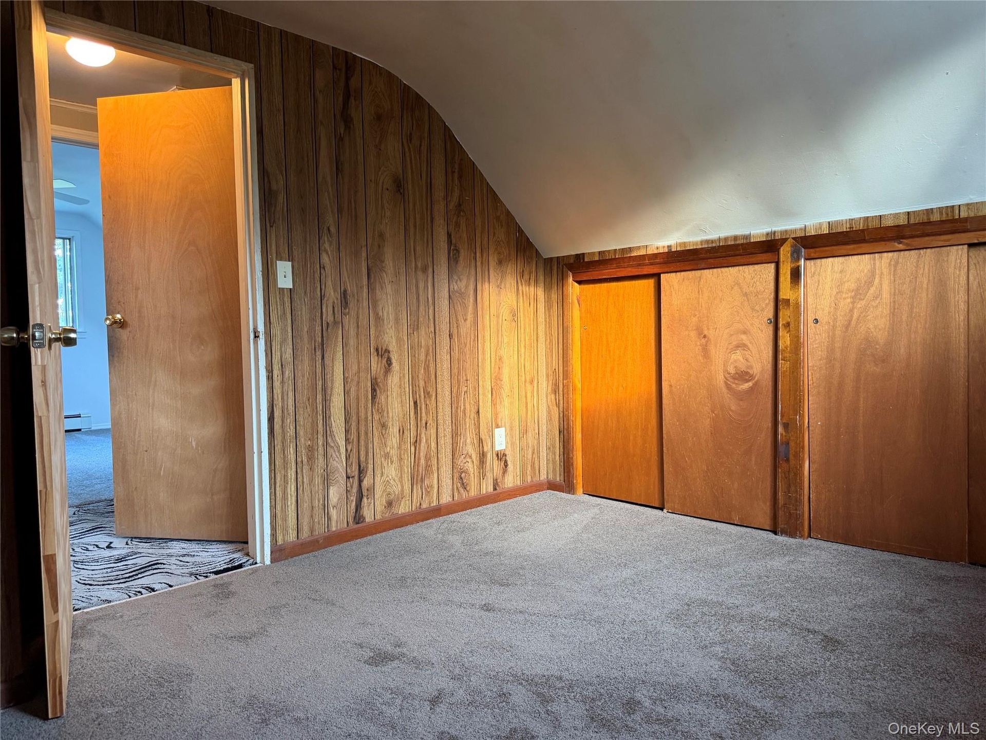 Sloped ceiling with recessed lighting, wood-finish wall paneling, and sliding wood-finish closet doors