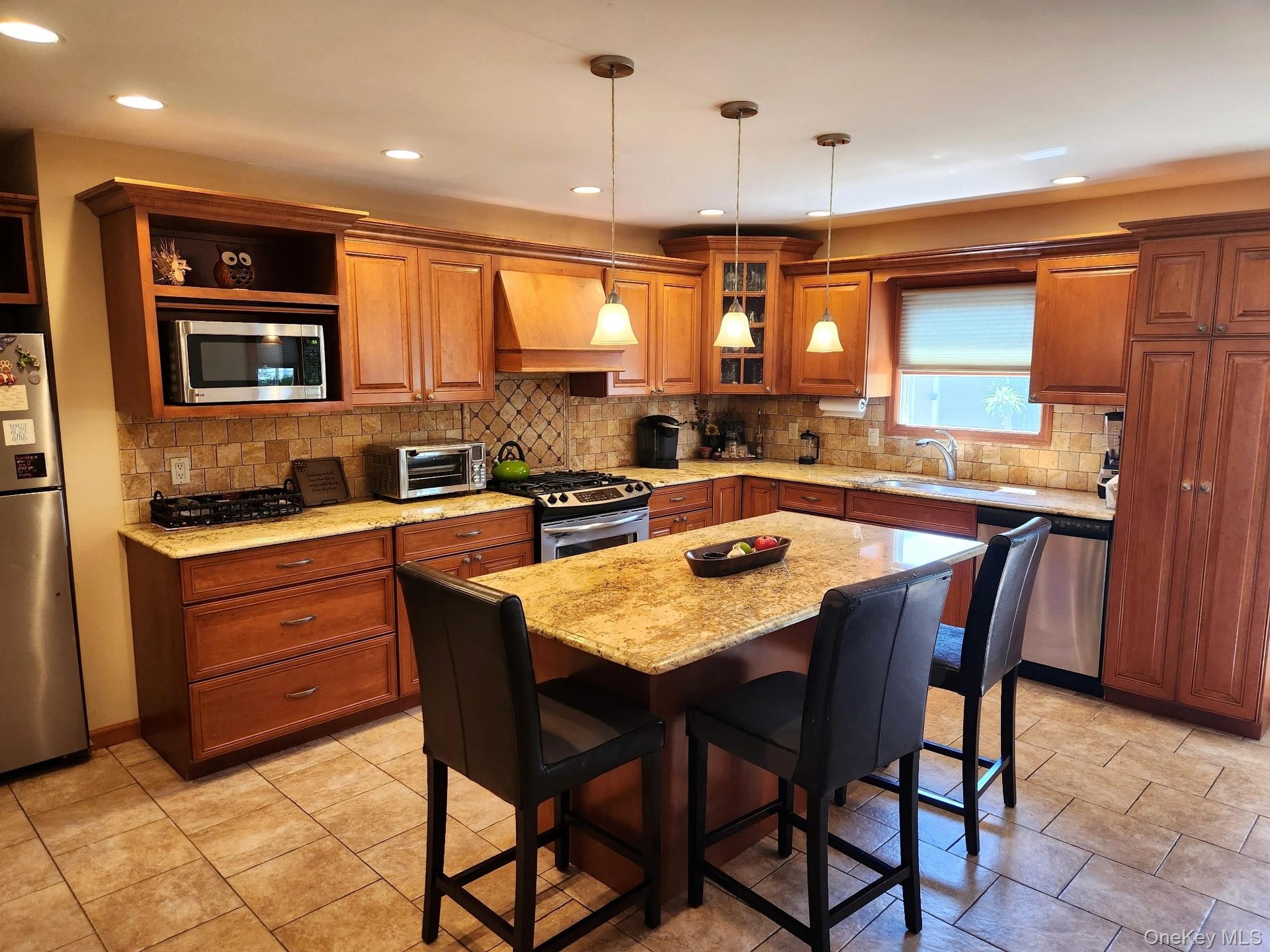 Wood-finish cabinetry with crown molding, stainless steel appliances, stone countertops, tiled backsplash, and recessed lighting