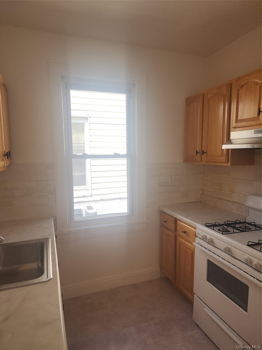 Kitchen featuring wood-finish cabinetry, white countertops, stainless steel sink, and a gas range