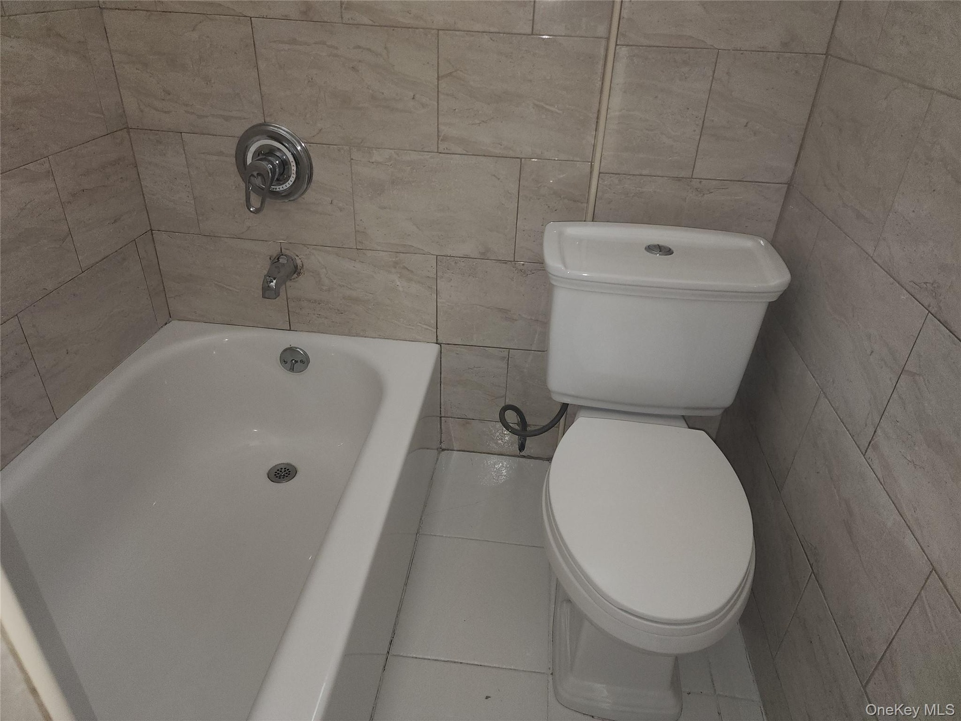 White porcelain bathtub with chrome fixtures and light-toned, rectangular wall tiling