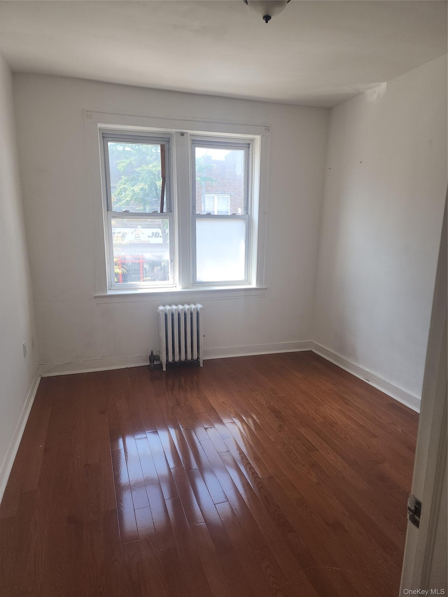 Hardwood flooring with a glossy finish, double windows with white trim, and a wall-mounted radiator