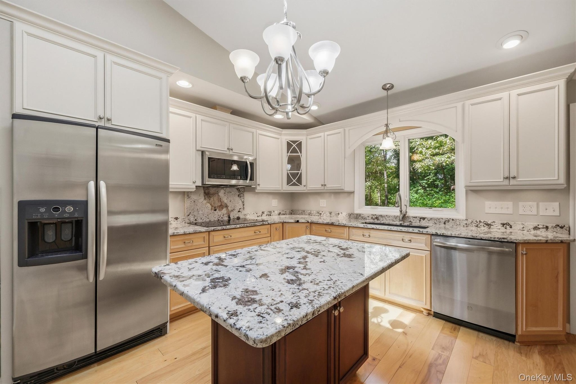 Custom kitchen with center island and snack bar, stainless appliances including double ovens, granite counters and wood floors