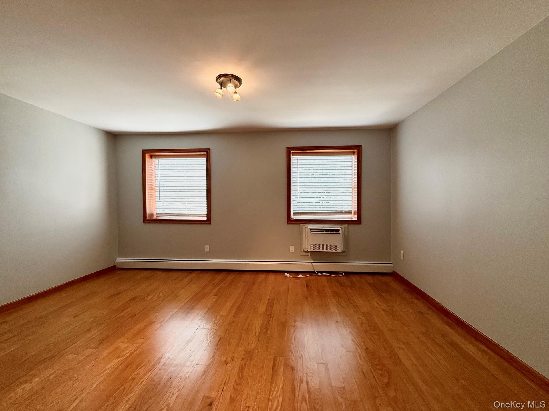 Hardwood flooring, painted walls, two windows with blinds, a window air conditioning unit, and a ceiling-mounted light fixture