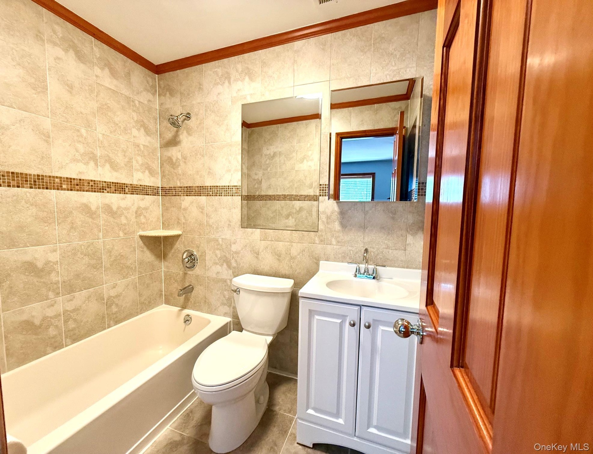 Full tiled bathroom with mosaic accent band, integrated bathtub, and white vanity with a single basin sink