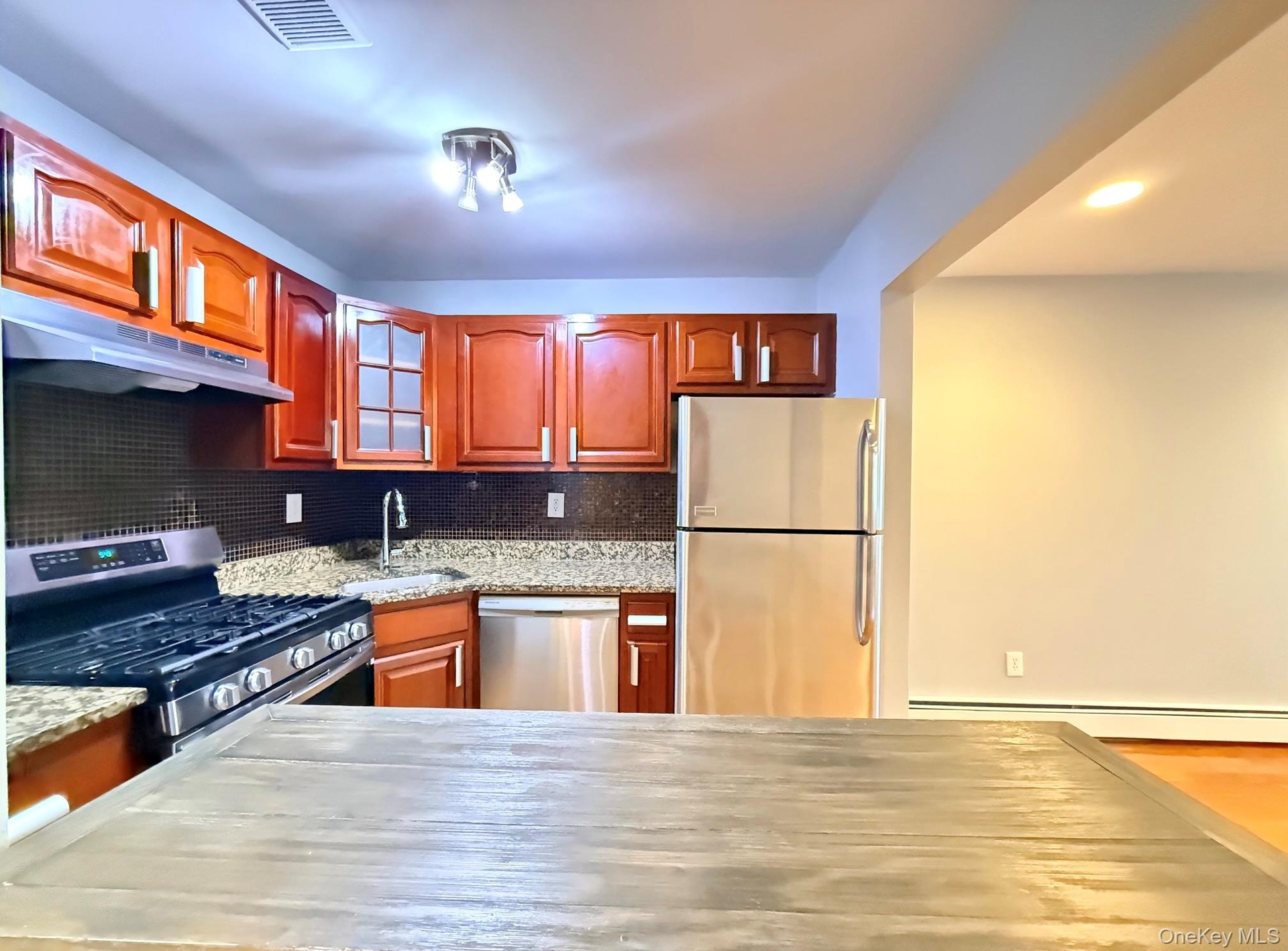 Kitchen featuring wood-finish cabinetry, stainless steel appliances, granite countertops, and a tile backsplash