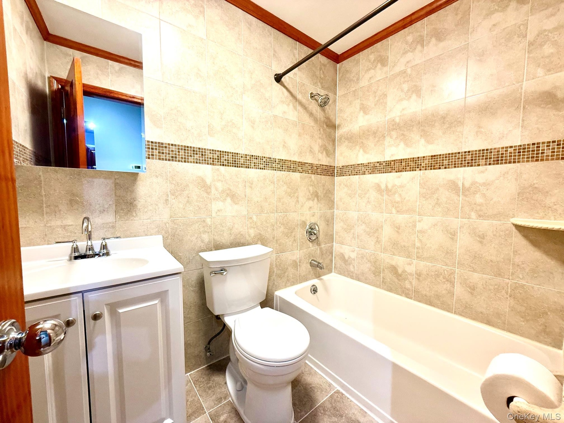 Tiled bathroom featuring a white vanity with integrated sink, chrome fixtures, a tiled shower, and mosaic accent tiling