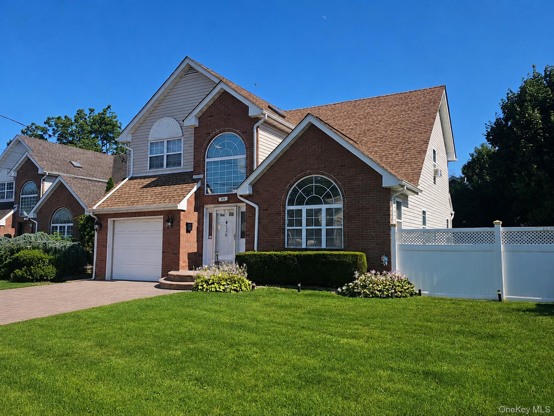 Brick and siding exterior with arched windows, attached garage, and a paver driveway