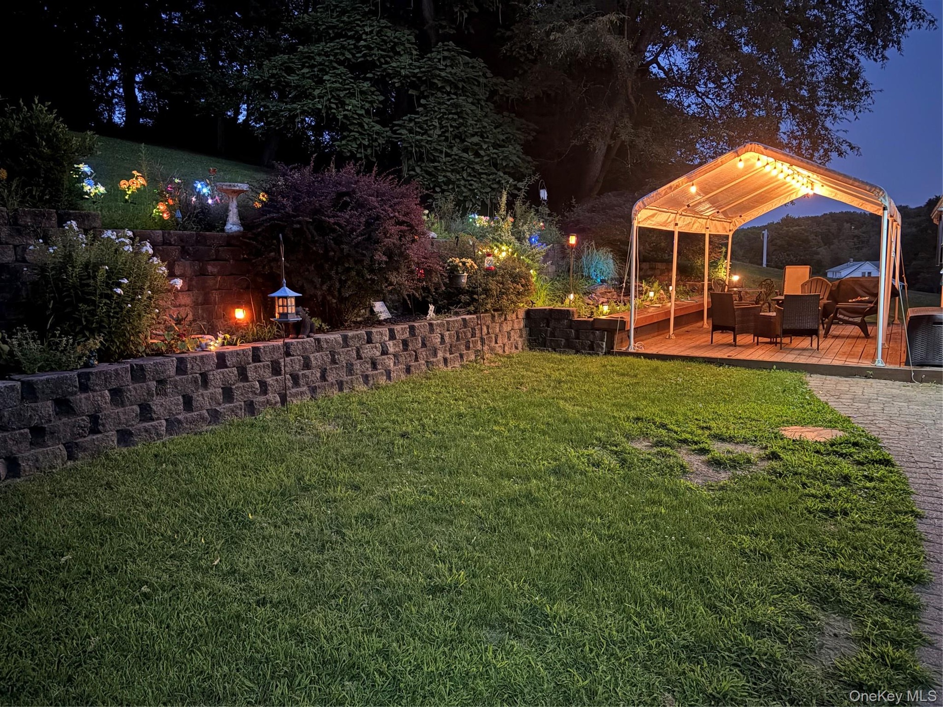 Lawn area with a block retaining wall, landscaped garden beds, and an illuminated covered deck
