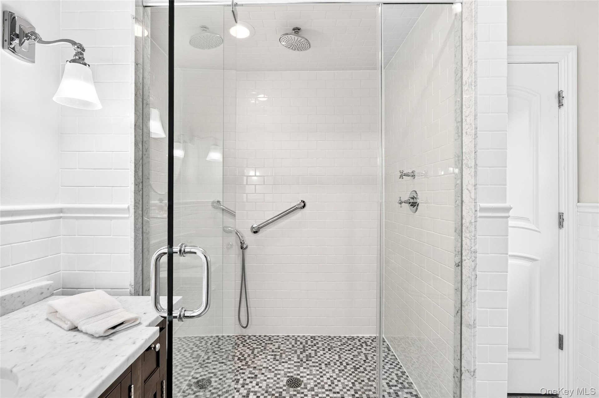 Glass-enclosed shower with subway tile walls, dual showerheads, and mosaic tile flooring