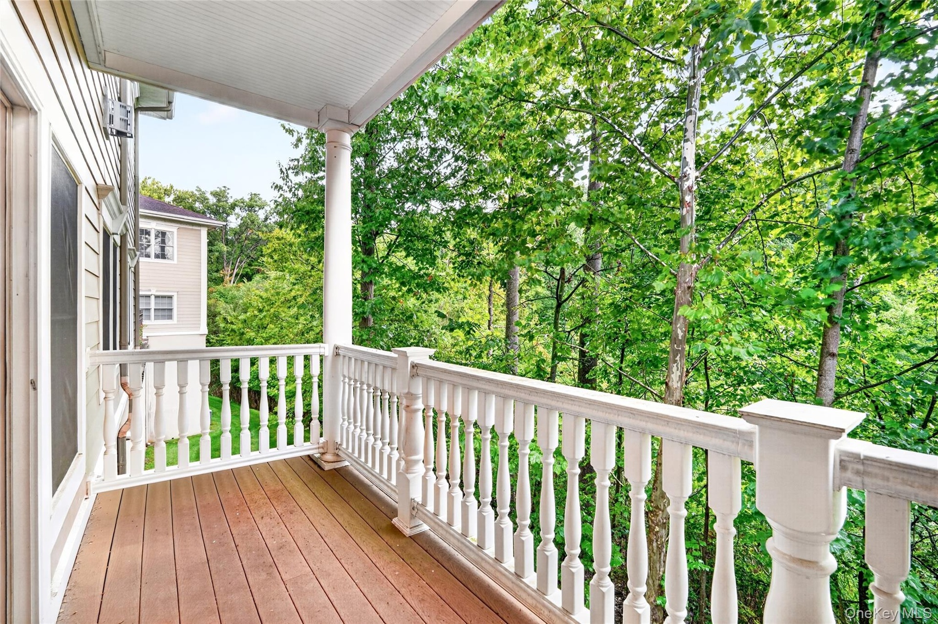 Outdoor balcony with wood-finish decking, white baluster railing, and a columned support