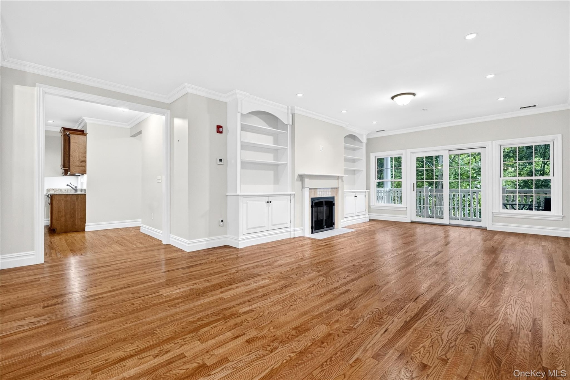 Hardwood flooring, white crown molding, built-in shelving, fireplace, and sliding glass doors to outdoor space