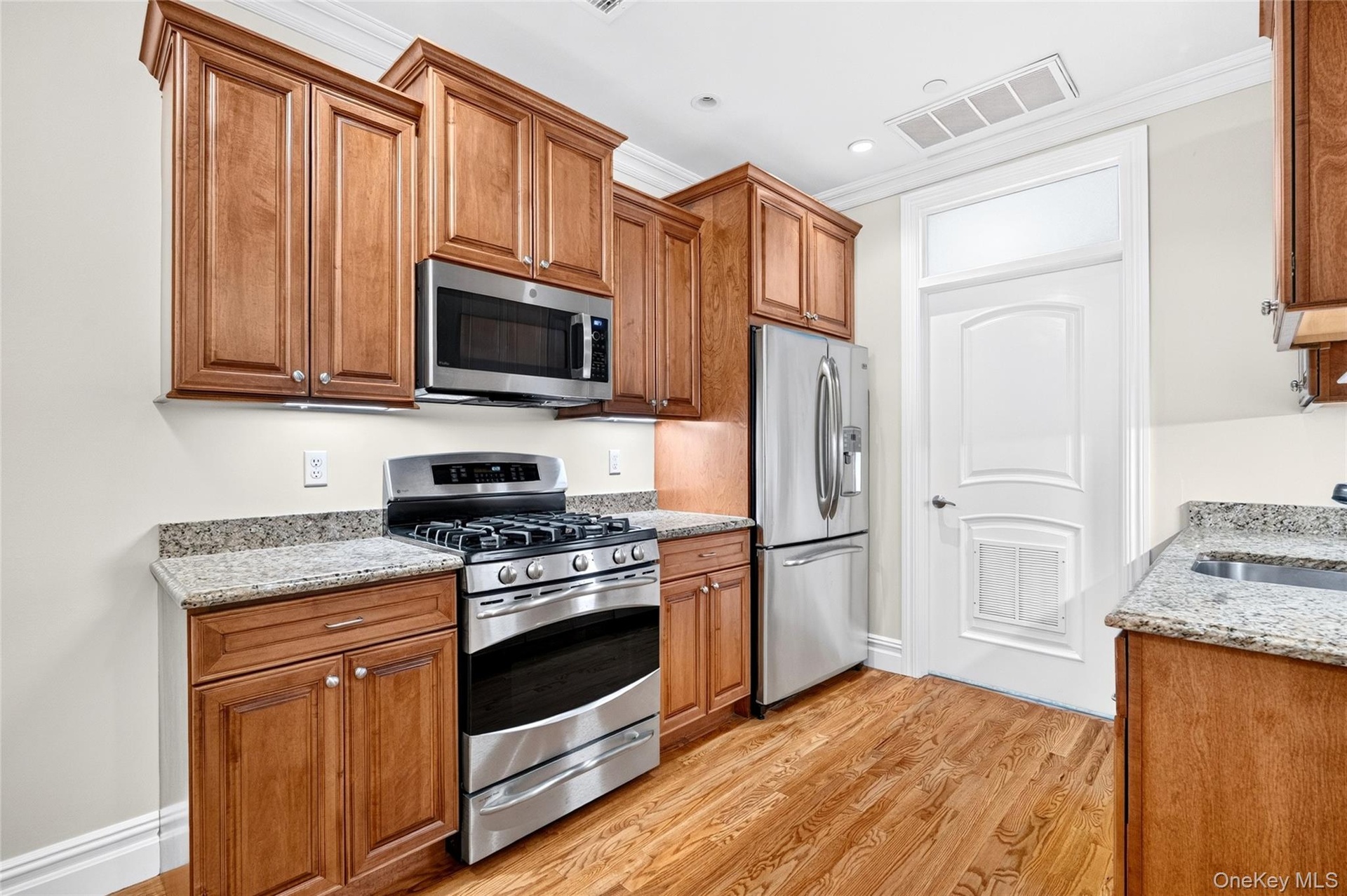 Kitchen featuring wood-finish cabinetry, stainless steel appliances, granite countertops, and wood-finish flooring