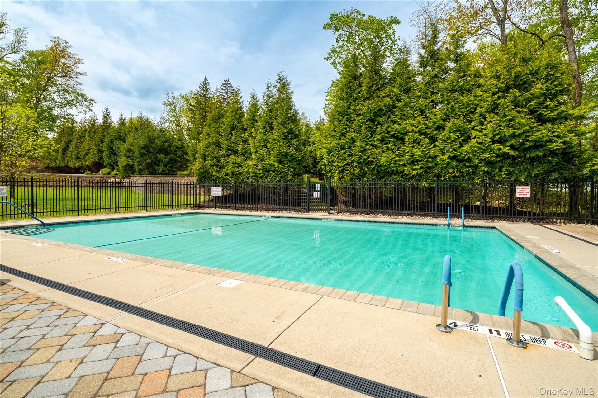 Fenced in-ground swimming pool featuring a concrete deck and a multi-toned paver patio