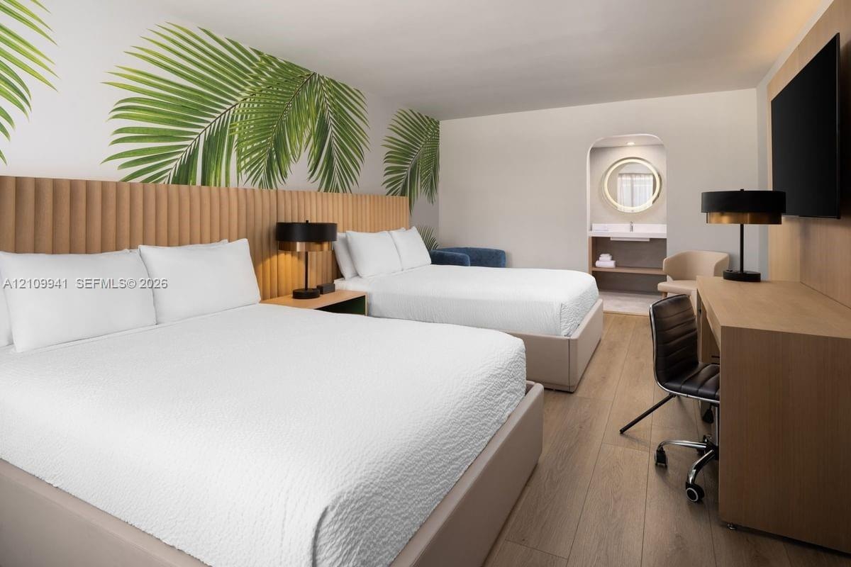 Room featuring wood-finish flooring, a vertical-slat built-in headboard, and an arched entryway leading to a vanity area with a circular LED-lit mirro