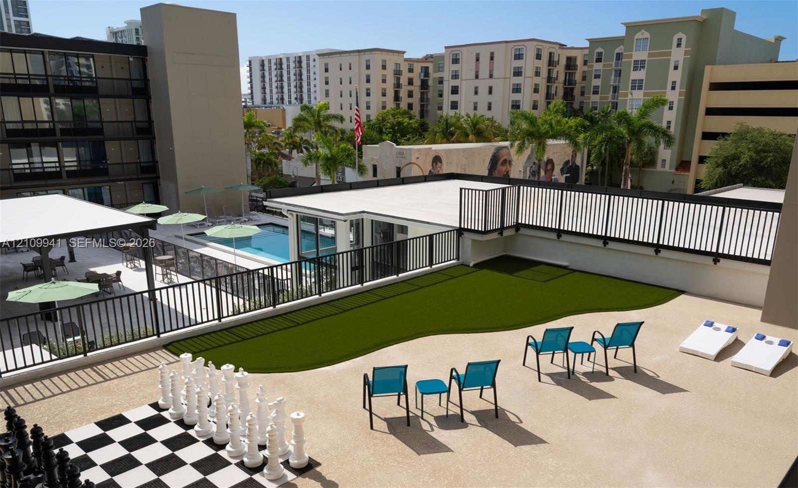 Elevated terrace featuring a synthetic grass lawn, oversized outdoor chess set, and black metal perimeter fencing
