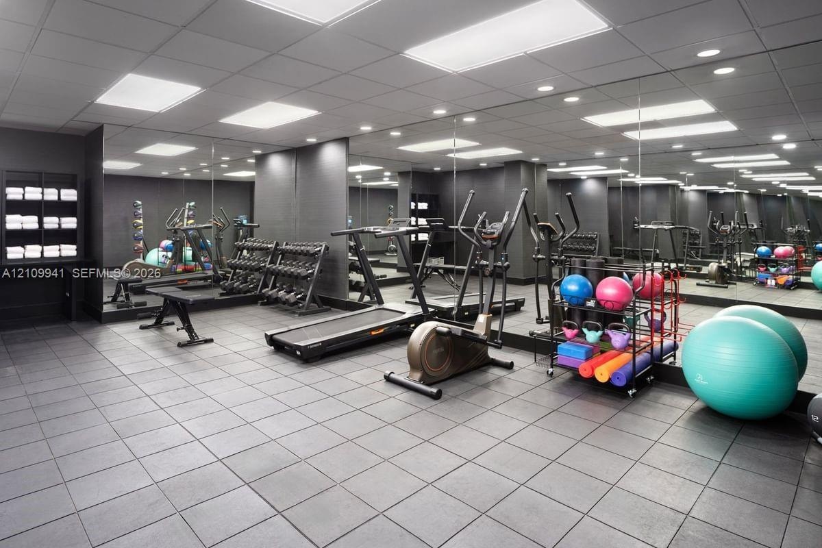 Fitness area featuring wall-to-wall mirrors, industrial-style tile flooring, recessed panel lighting, and built-in storage shelving