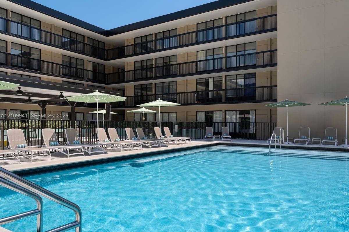 Swimming pool with integrated stainless steel ladder, expansive concrete deck, metal perimeter fencing, and multi-story building facade featuring priv
